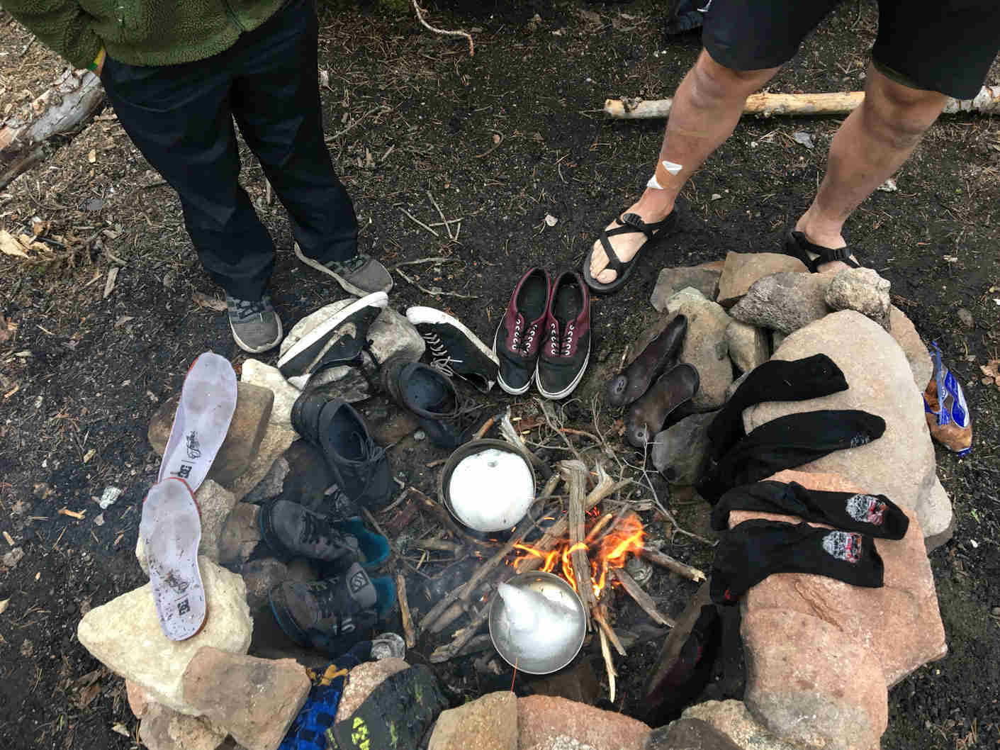 Downward view of shoes and socks on the rocks around a campfire