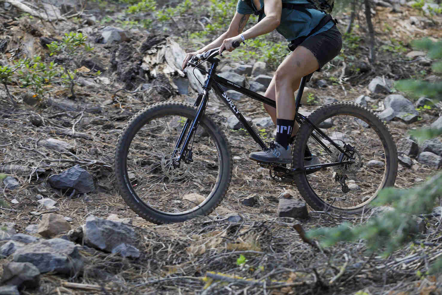 Left side view of a cyclist on a Surly Karate Monkey bike, black, across a rocky hill in the forest