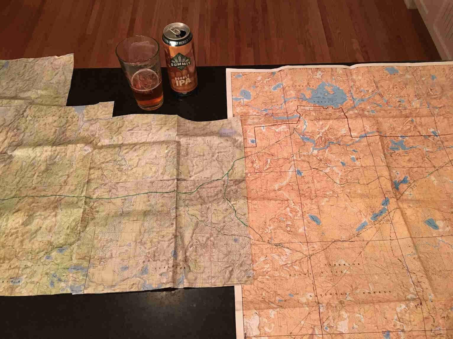 Downward view of two maps, a glass of beer and can, on a table top