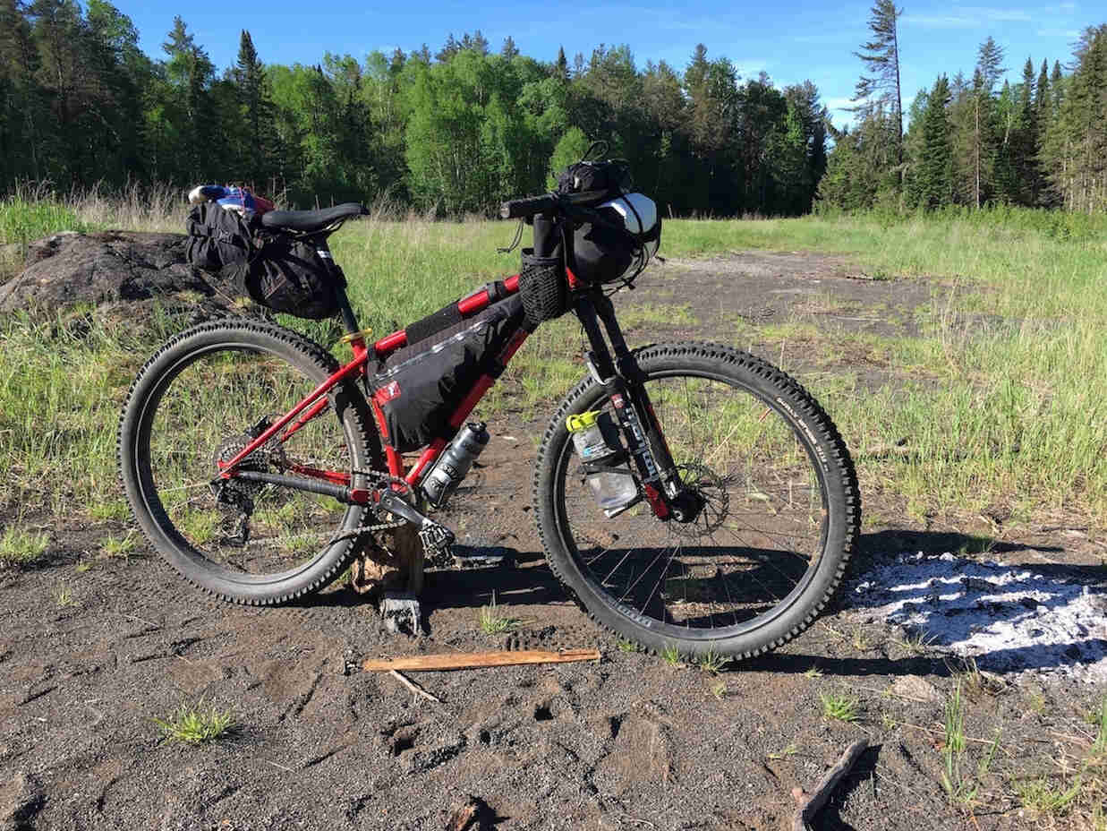 Right side view of a Surly bike, red, on a patch of red gravel in a grassy field, with trees in the background