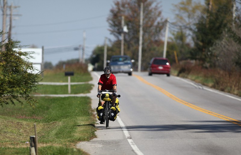 Front view of a cyclist riding down paved road shoulder on a Surly Long Haul Trucker bike loaded with gear