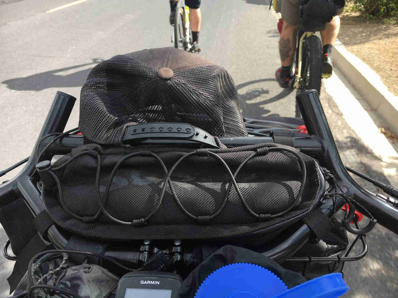 Downward close up of the handlebars loaded with gear on a bike with other cyclist in front view
