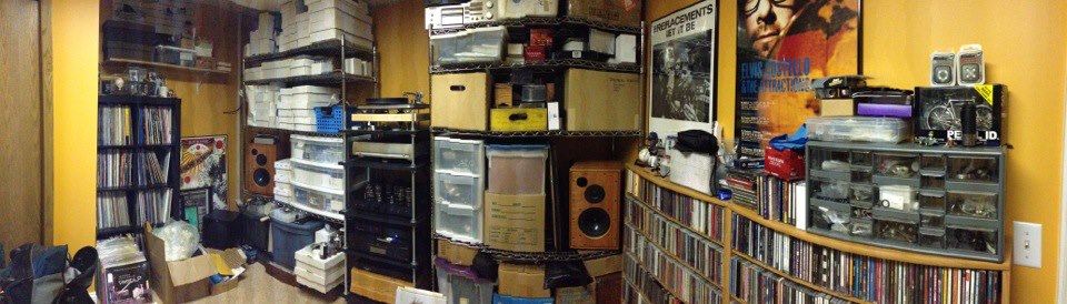 Panoramic view of an interior room, with shelves loaded with record albums and stereo equipment, against the walls