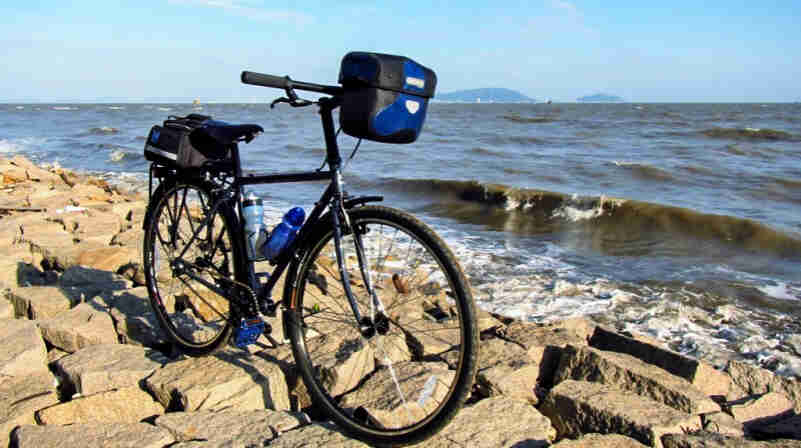Front right side view of a black Surly Cross Check bike, parked on a rocky back of the sea