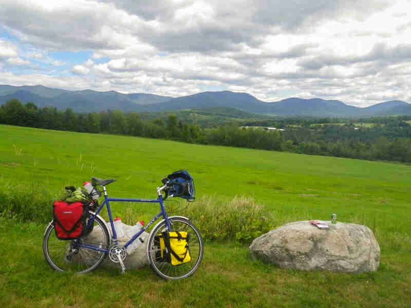 Right side view of a blue Surly Long Haul Trucker parked in a grassy field, with trees and mountain in the background