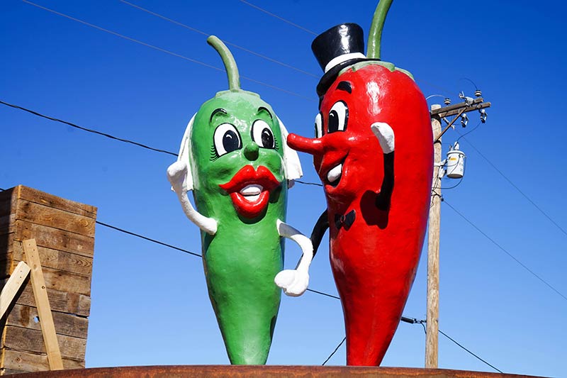 A statue of green and red peppers on a platform with power lines and blue sky behind
