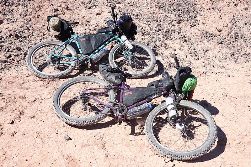 Two Surly bikes loaded with gear, laying on their left side in the sand