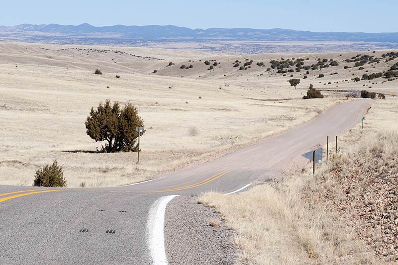 A winding two lane highway plains grass with mountain hills in the distance