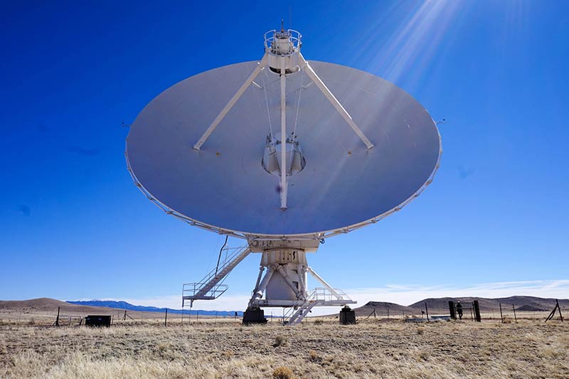 A very large white satellite set up in a field of desert plains on a bright, sunny day