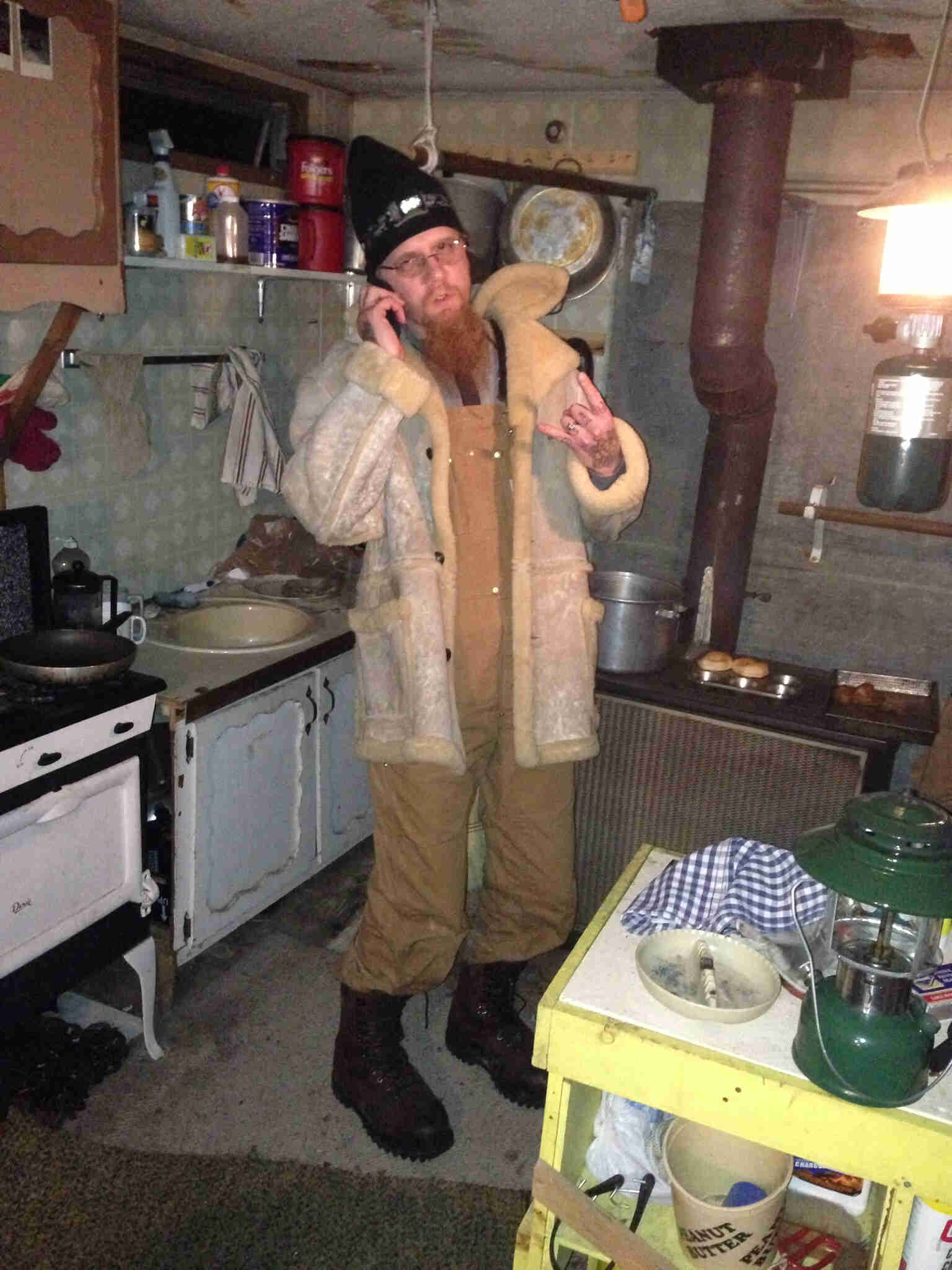 Front view of a person standing in a hunting shack cabin, with their left hand pointer and pinky fingers sticking up