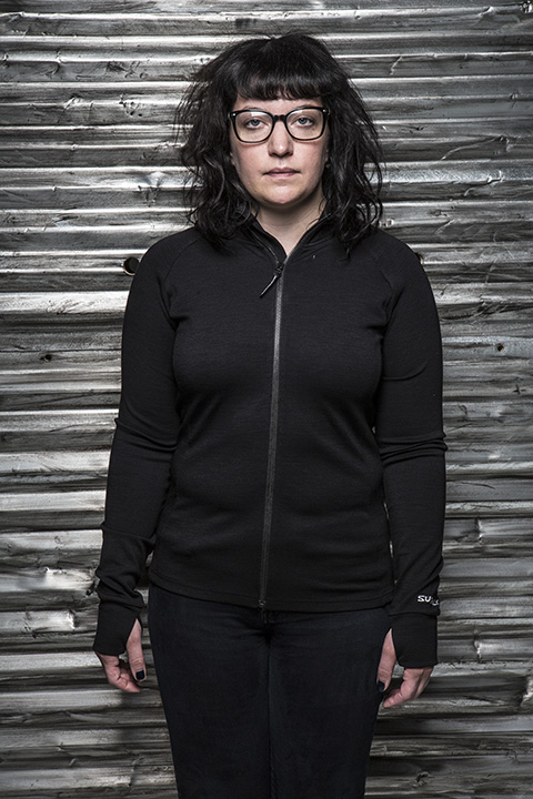 Front view of a person wearing a black wool zip up jacket in front of a corrugated steel wall