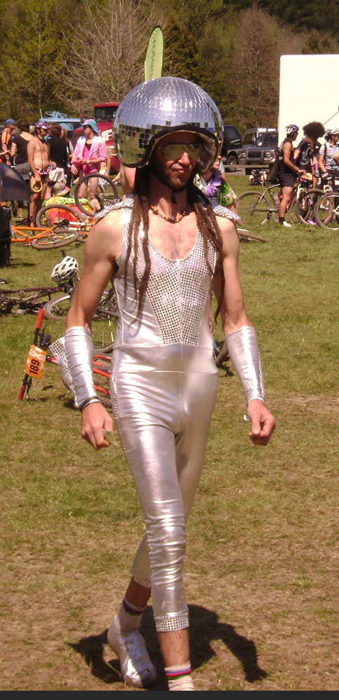 Front view of a person wearing a disco ball helmet and a silver jumpsuit, with people in the background