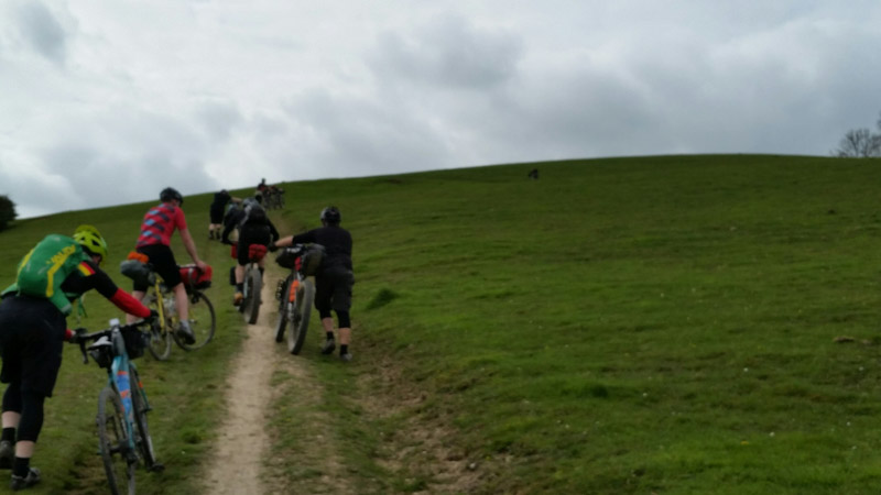 Rear view of cyclists walking their bikes up a hill on a pasture road