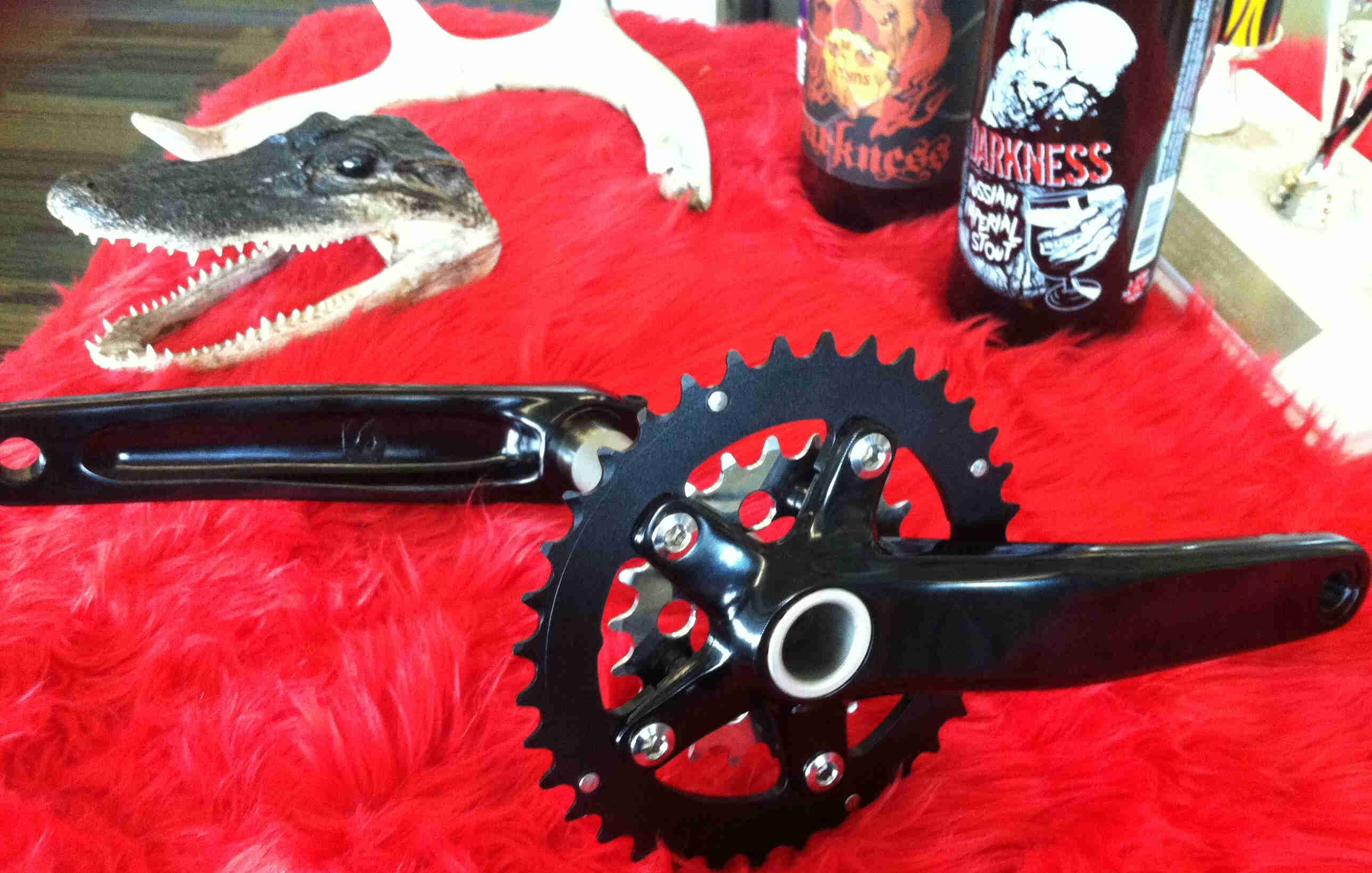 Side view of a Surly O.D bike crankset, on a red table with an alligator head and cans in the background