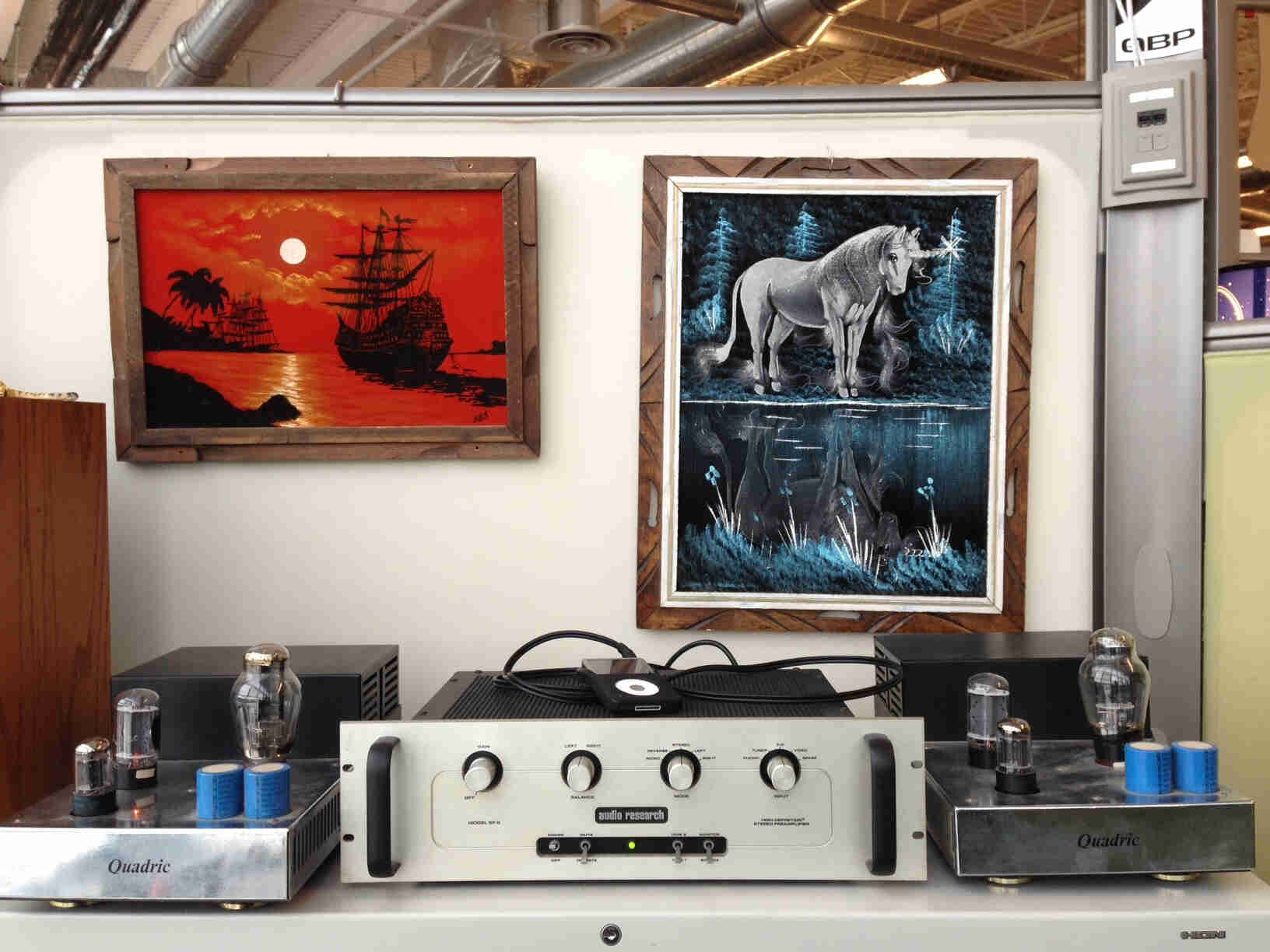 Front view of audio equipment, sitting on a table in an office cubicle, with framed paintings on the wall behind it