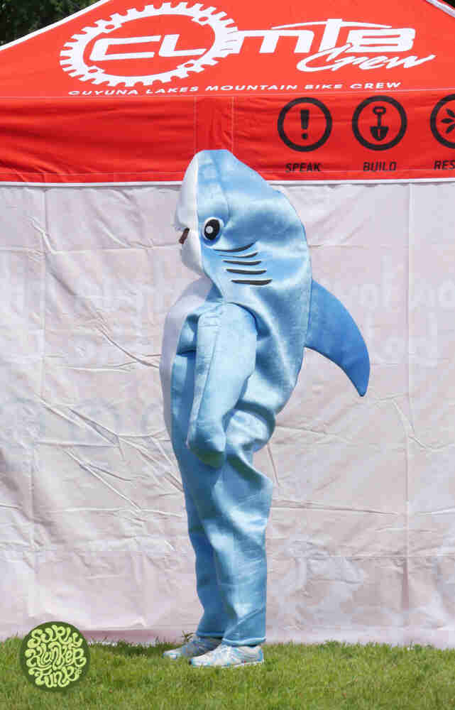 A person wearing a shark costume, standing next to a CLMRC canopy