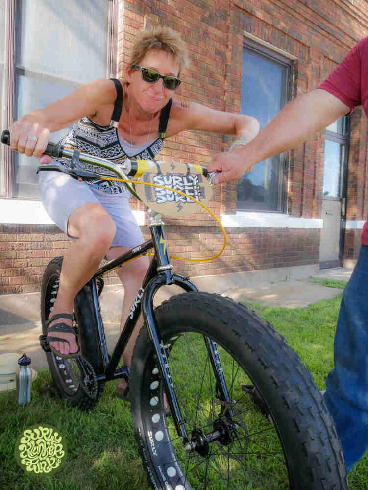 Front view of a cyclist on a Surly Pugsley fat bike, next to a building, with a person holding them up by the handlebar
