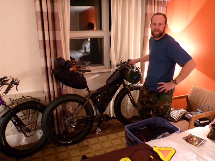 Right side view of a Surly Moonlander bike fat bike with gear, against a motel room wall, with a person standing near