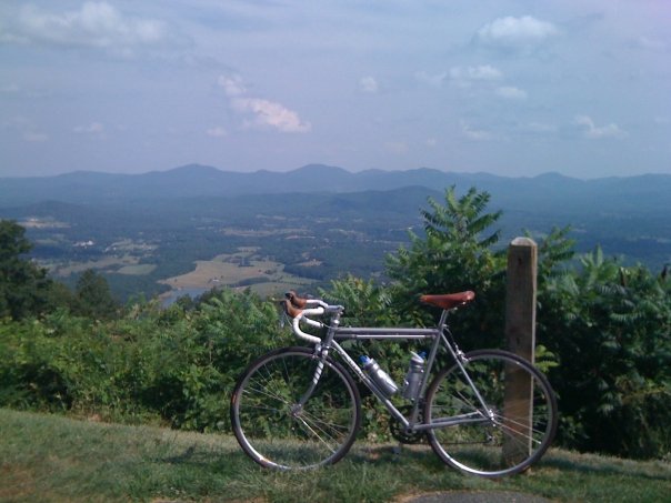 Left side view of a Surly Pacer bike, white, on the grass at an overlook with trees and mountains behind