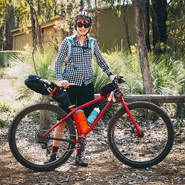 Right side view of a red Surly bike with gear packs and a cyclist standing behind, in the woods