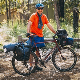 Right side view of a dark red Surly bike with gear packs and a cyclist standing behind, in the woods