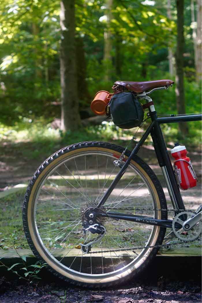 Right side view of the back half of a Surly Pack Rat bike with gear, in the woods