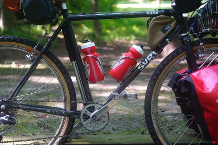 Right side view of a Surly Pack Rat bike loaded with gear, on a gravel trail in the woods
