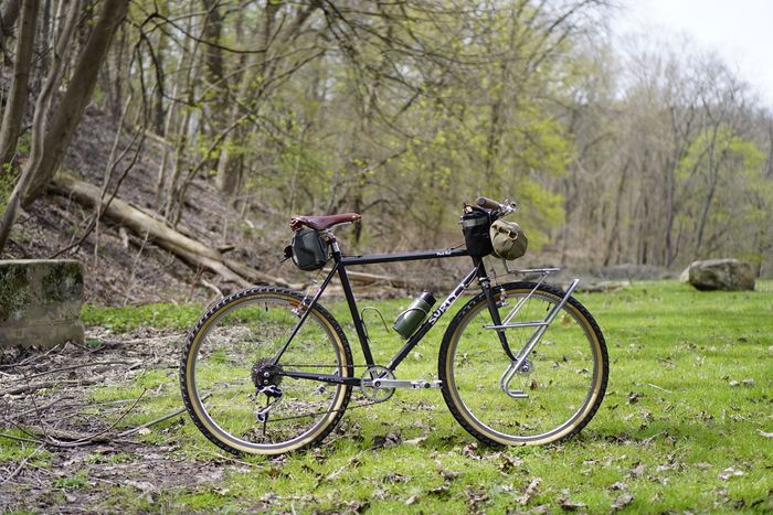 Right side view of Surly Pack Rat bike in the grass with a tree covered hill to the left
