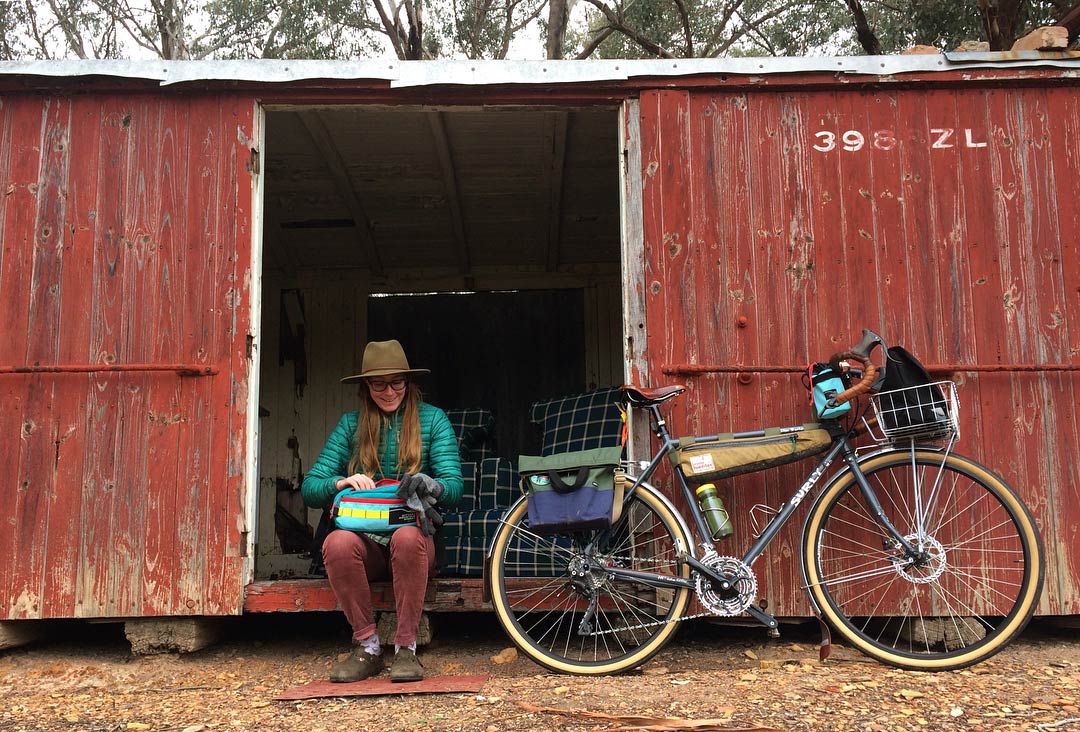 Person sitting at the door  opening of a red steel shed with their Surly bike next to them