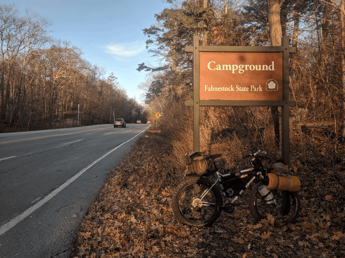 Right side view of a white Surly Pugsley fat bike leaning of a Fahnestock State campground sign beside paved roadway