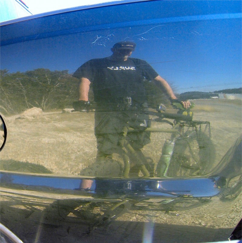 A reflection on a black truck bed, showing a person standing next to a Surly Pugsley Ops fat bike