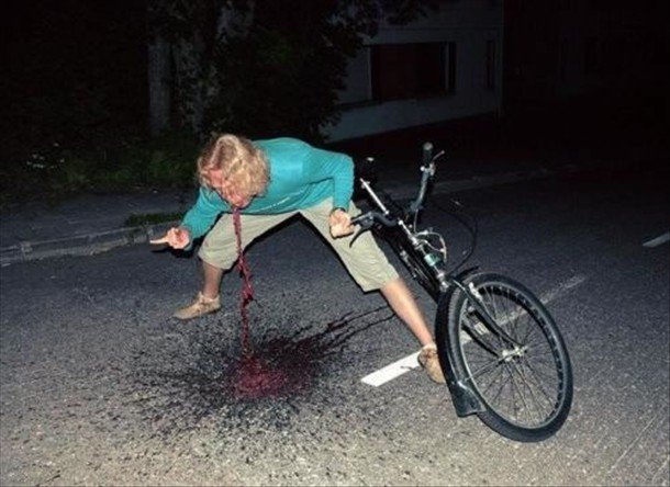 Front view of a person leaning over and throwing up, with a bike leaning on them, on a street at night