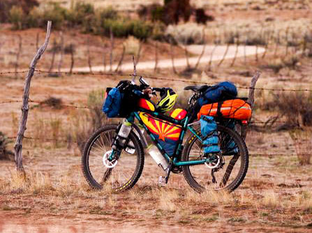 Left side view of a Surly Troll bike, loaded with gear, standing in desert grass, with a road in the background