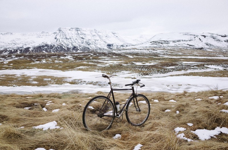 Rear, right side view of a black Surly bike, in a field of brown, flowy grass and snow, facing snowy mountains