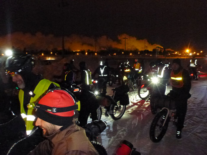 A group of winter cyclist and their bikes, standing on a snow covered road at night
