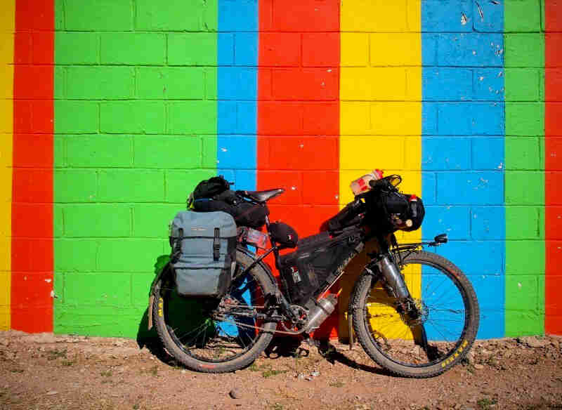 Right side view of a Surly Troll bike, loaded with gear, leaning against a color strip cinder block wall