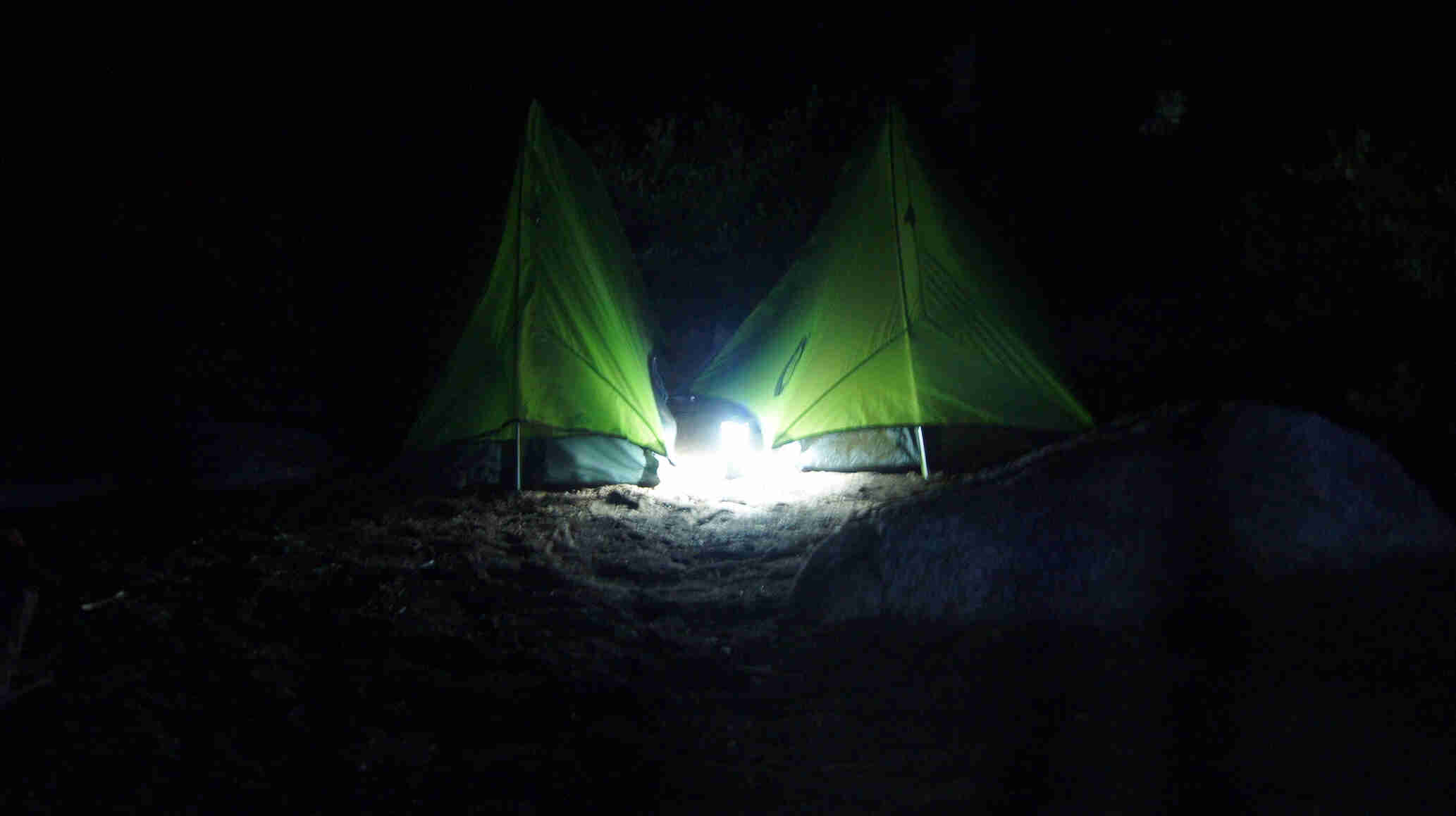 Two tents, next to each other, at night, with a light on the ground between them