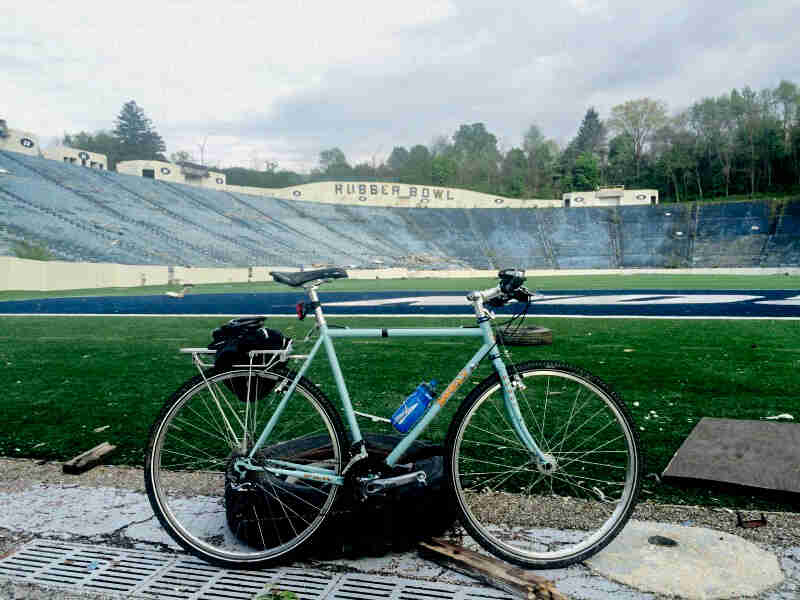 Right side view of a mint Surly Cross Check bike, parked inside an empty football stadium