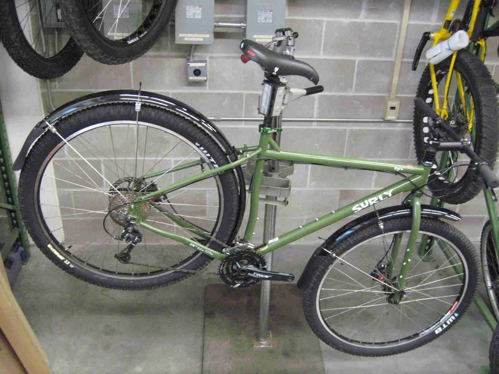 Right side view of a green Surly Ogre bike with fenders, mounted to a bike repair stand, inside a workshop room