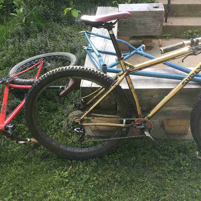 Two Surly Krampus bikes and one frame, on the grass next to a wood beam porch deck