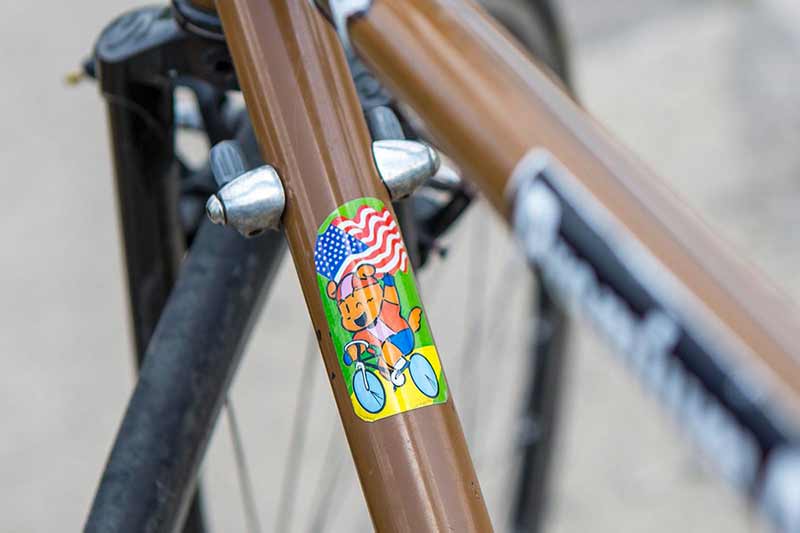 茶色の Surly 自転車、アメリカ国旗を持って片手で自転車にのる動物のイラストのステッカーが貼られたダウンチューブのアップ