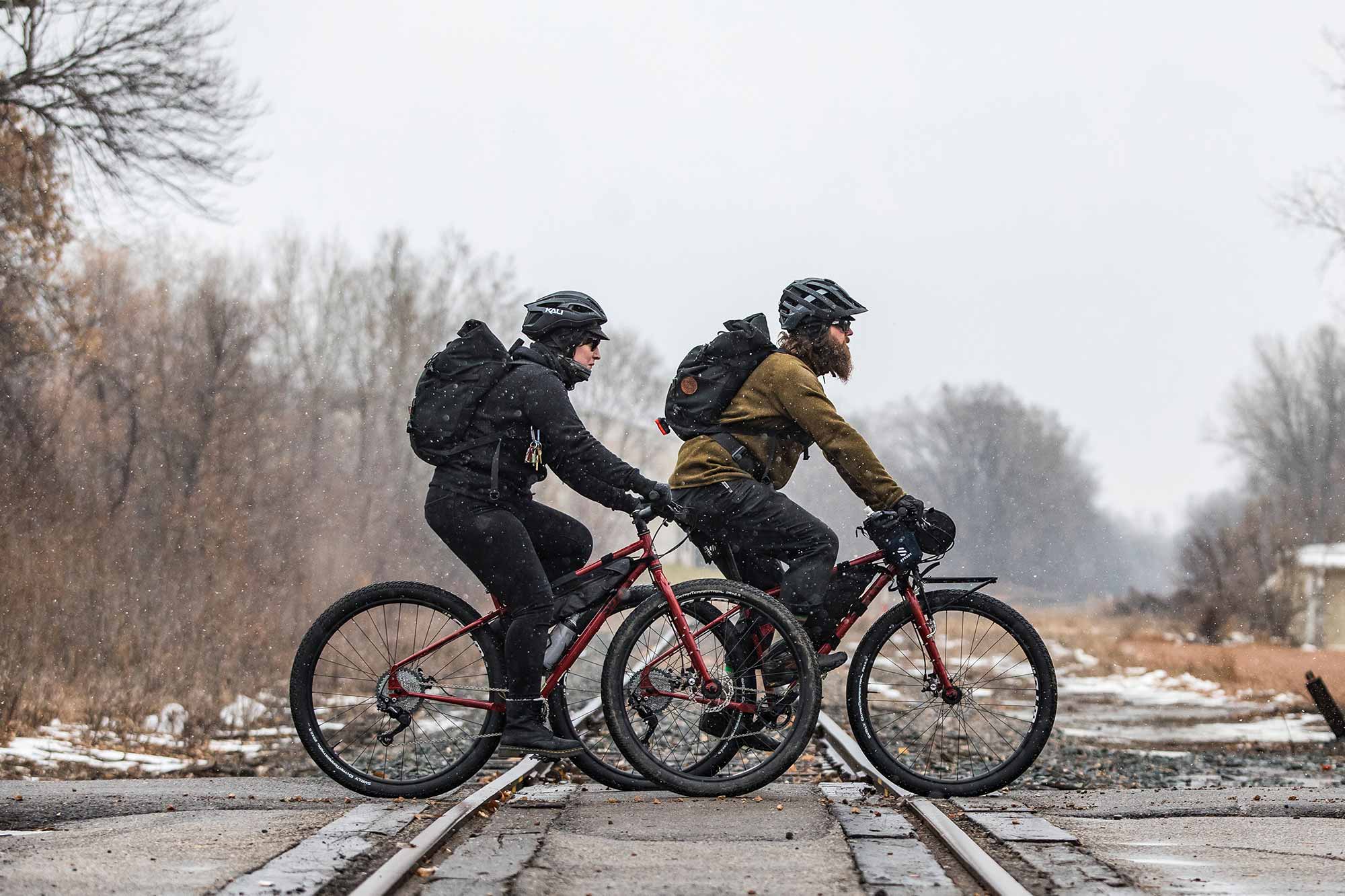 小雪が降る中を、暖かい服、ヘルメット、バックパックを身につけて通勤する 2 台の自転車