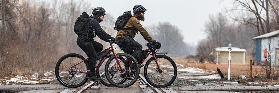 小雪が降る中を、暖かい服、ヘルメット、バックパックを身につけて通勤する 2 台の自転車