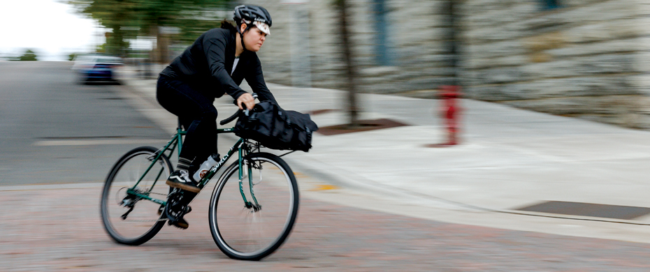 Cyclist riding a black Surly Pack Rat bike, leans into a left turn at the bottom of a hill on a city street