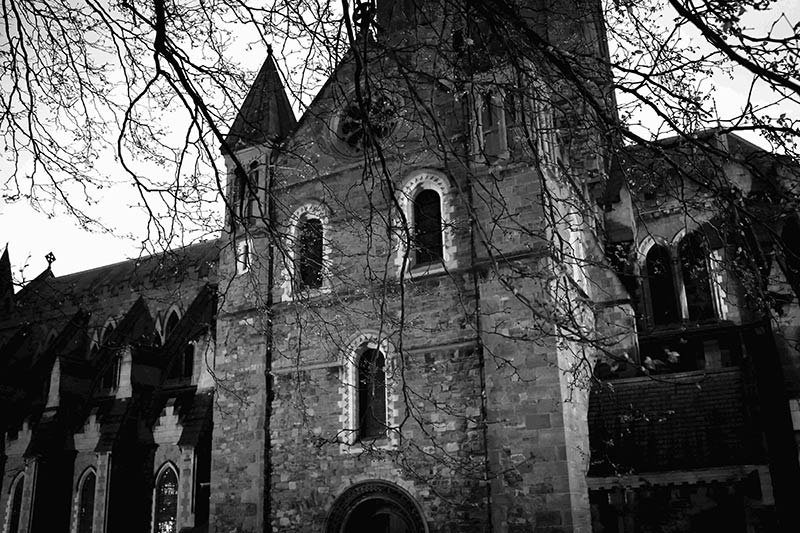 Black & white image of the outside of a church, with bare tree branches hanging down in front