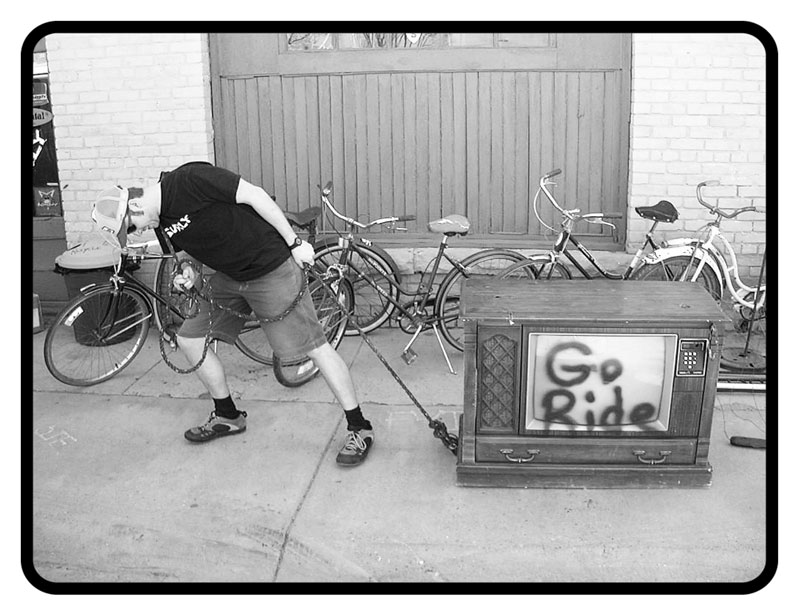 Person pulling a tube TV across a sidewalk, with bike lined up in front of a building in the background