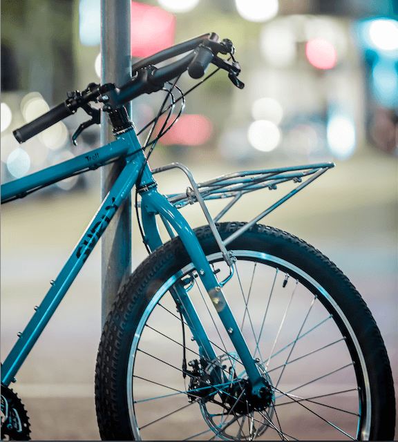 Surly Troll bike - turquoise - with 24-Pack Rack - parked against a steel pole - cropped, right side, front end view
