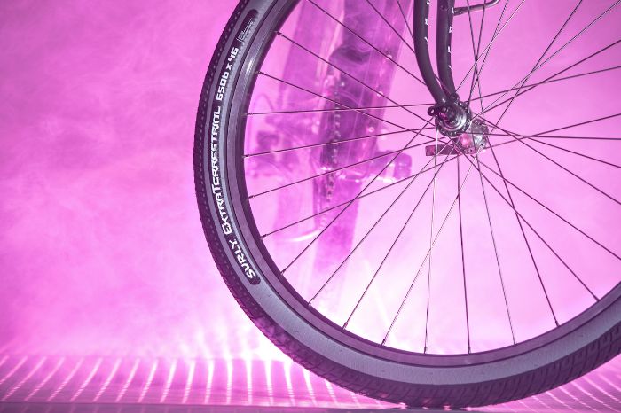 Profile of a Surly Extra Terrestrial bike tire with gray slate sideways mounted on rim with spokes and lavender spoke and lights in the background