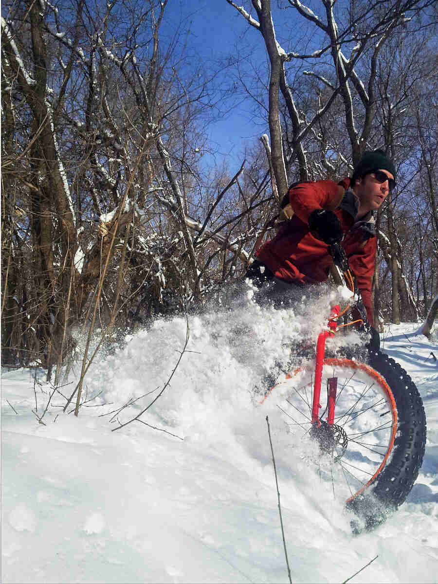 A cyclist, riding a red Surly Pugsley fat bike, thrashes through deep snow in the woods