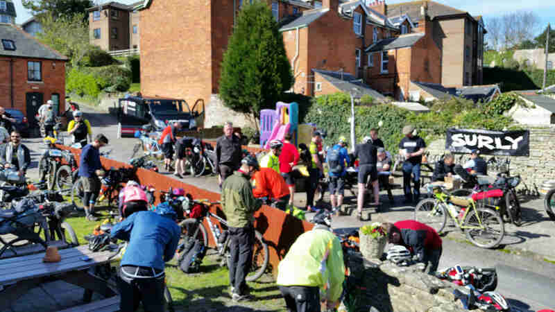 A group of cyclist stand around with their bikes, with a Surly banner and buildings in the background